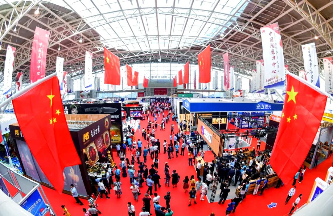 An aerial view of a crowded exhibition hall at the China (Yangjiang) International Hardware, Knives and Scissors Fair, hung with red national flags